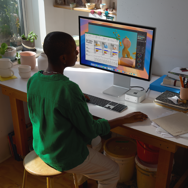 Person at a desk using a Mac mini and display to work in apps with colorful screen activity